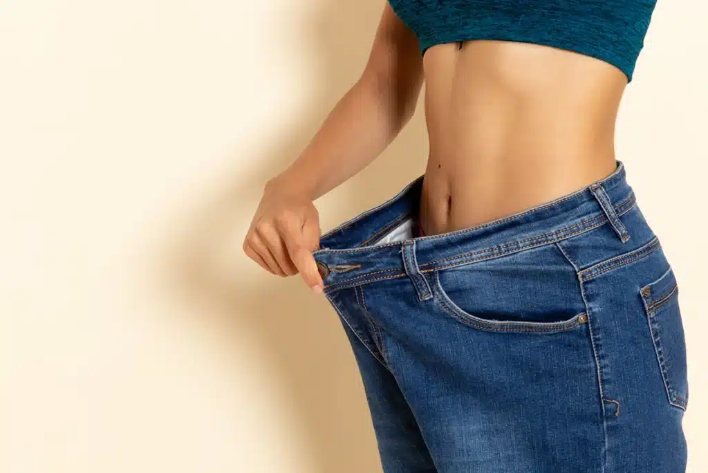 ront view of young female with fit body in shirt and jeans on white wall